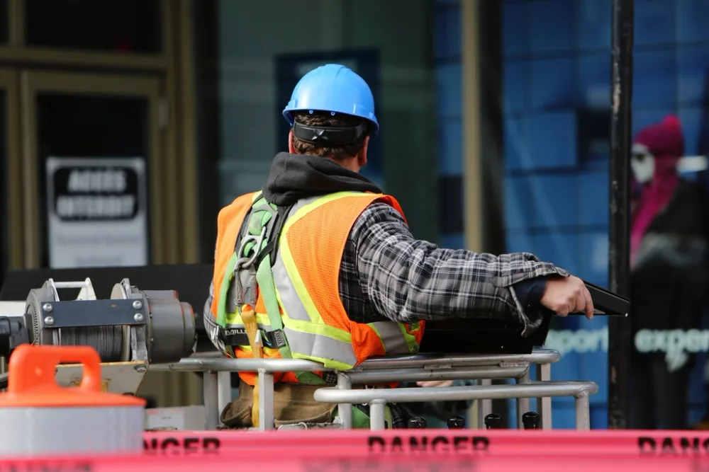 Construction worker in a hard hat, high visibility vest and safety harness behind danger tape